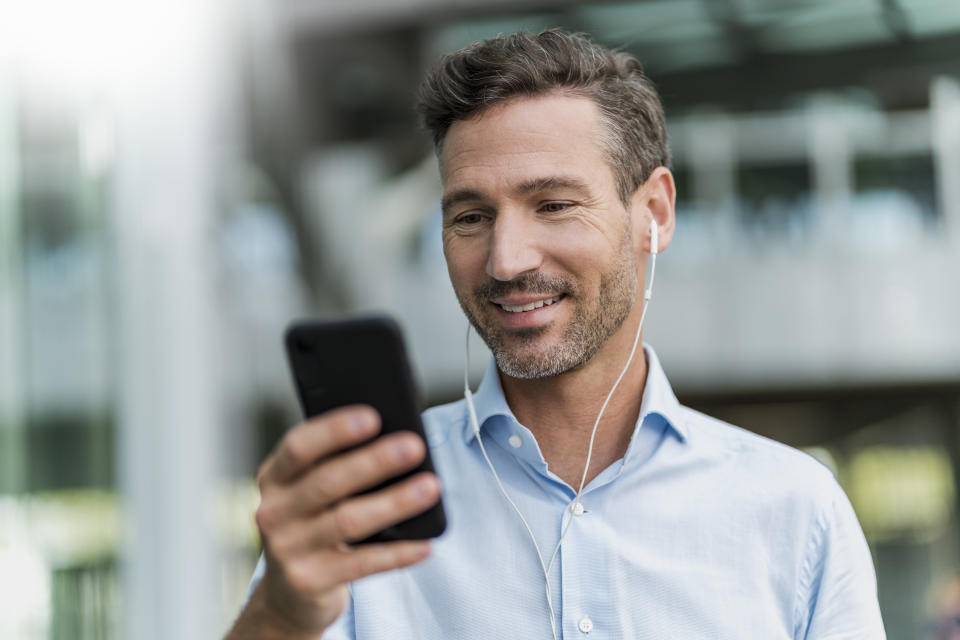 Smiling businessman with earphones and cell phone in the city