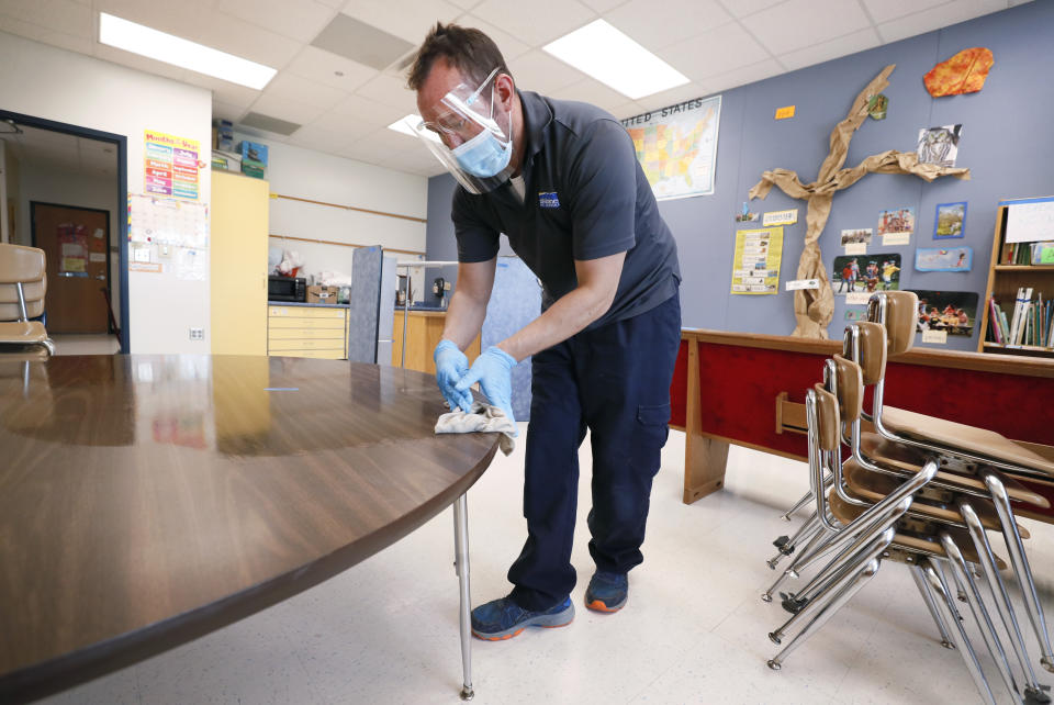 Des Moines Public Schools custodian Joel Cruz cleans a desk in a classroom at Brubaker Elementary School, Wednesday, July 8, 2020, in Des Moines, Iowa. School districts that plan to reopen classrooms in the fall are wrestling with whether to require teachers and students to wear face masks. In Iowa, among other places, where Democratic-leaning cities like Des Moines and Iowa City have required masks to curb the spread of the coronavirus, while smaller, more conservative communities have left the decision to parents. (AP Photo/Charlie Neibergall)