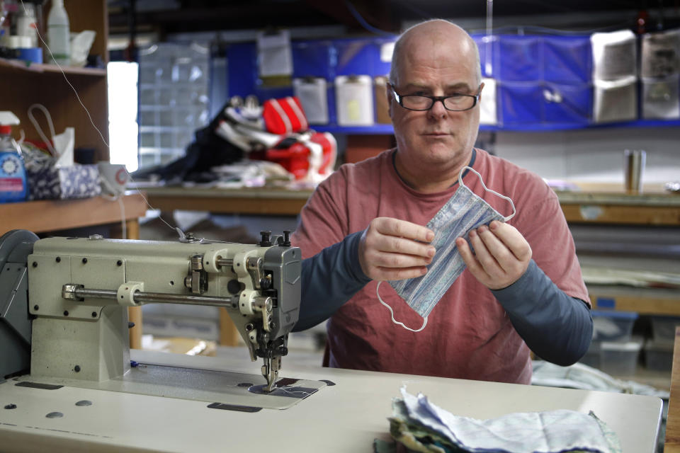 In this Monday, March 23, 2020 photo, Eric Baldwin examines the stitching on a cotton mask, one of hundreds he and the employees at his sail-maintenance business are making for caregivers during the coronavirus outbreak, at his shop in Freeport, Maine. (AP Photo/Robert F. Bukaty)