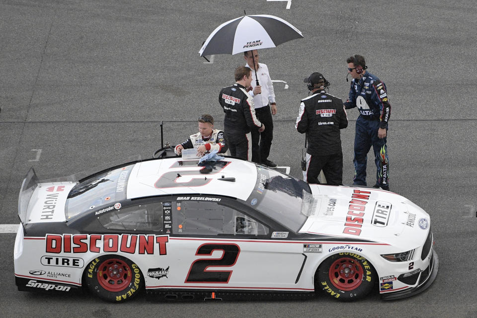 Brad Keselowski stands under an umbrella on pit road as rain forces a red flag during the NASCAR Daytona 500 auto race at Daytona International Speedway, Sunday, Feb. 16, 2020, in Daytona Beach, Fla. (AP Photo/Phelan M. Ebenhack)