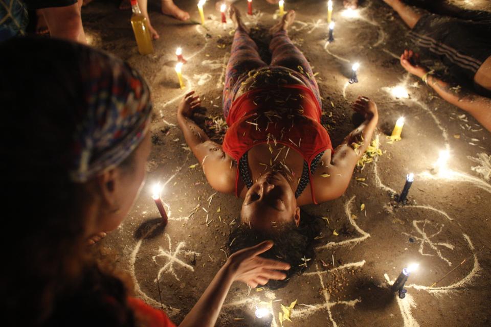 In this photo taken Oct. 11, 2019, a woman surrounded by candles and designs drawn on the ground with white powder lies with her eyes closed during a spiritual ceremony on Sorte Mountain where followers of indigenous goddess Maria Lionza gather annually in Venezuela's Yaracuy state. Believers often ask for spiritual healing or protection from witchcraft, or thank the goddess for curing an illness. (AP Photo/Ariana Cubillos)