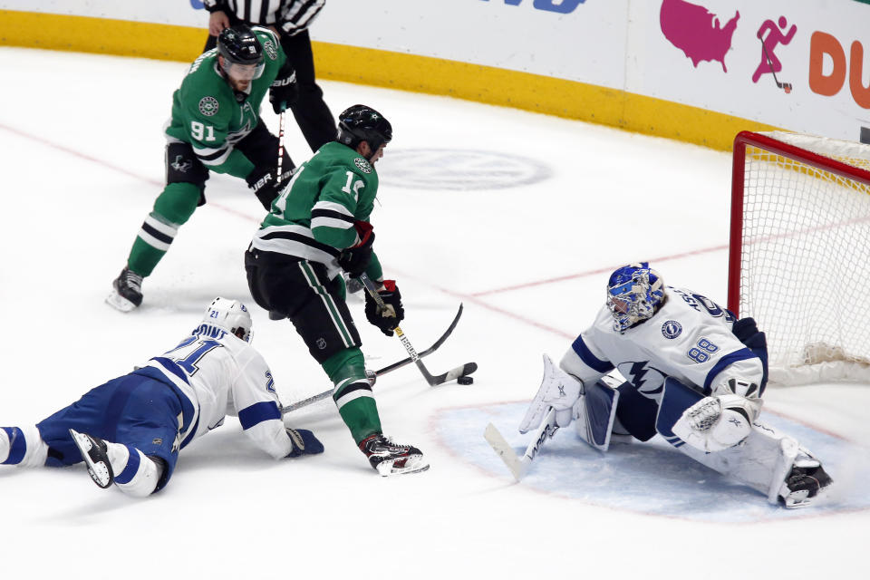 Dallas Stars left wing Jamie Benn, center, skates past Tampa Bay Lightning center Brayden Point, left, and shoots the game winning goal past goaltender Andrei Vasilevskiy, right, during overtime of an NHL hockey game in Dallas, Monday, Jan. 27, 2020. (AP Photo/Ray Carlin)