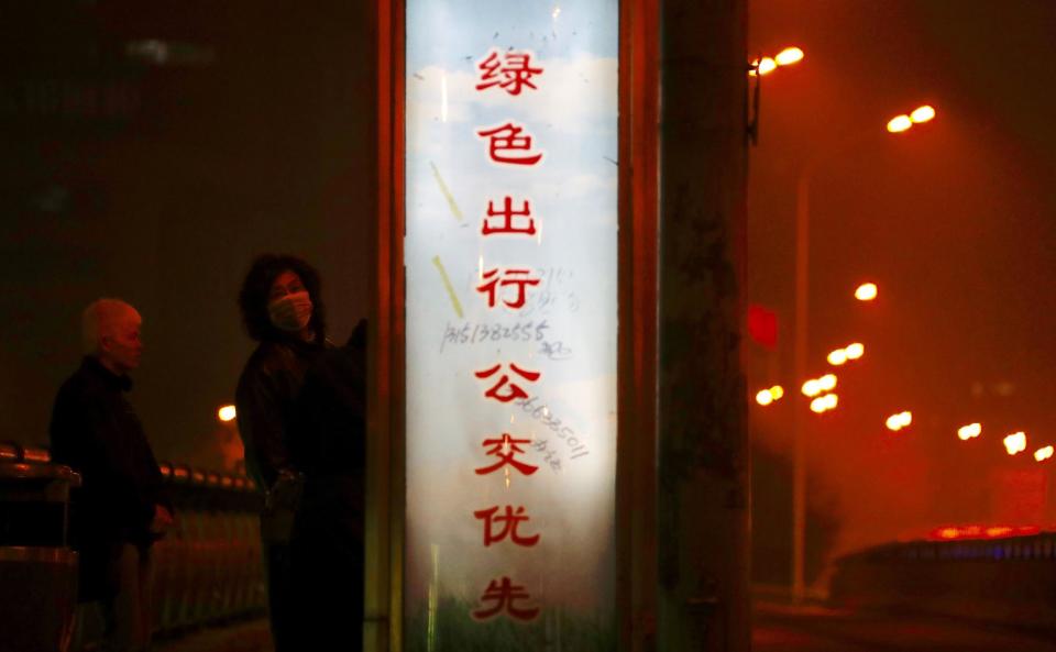 In this Monday, Jan. 2, 2017 photo, a pedestrian wearing a mask looks back while passing by a slogan that reads: "When you want to go out, please take a public bus" in Beijing. Beijing and other cities across northern and central China were shrouded in thick smog on Monday, prompting authorities to delay dozens of flights and close highways. (AP Photo/Andy Wong, File)