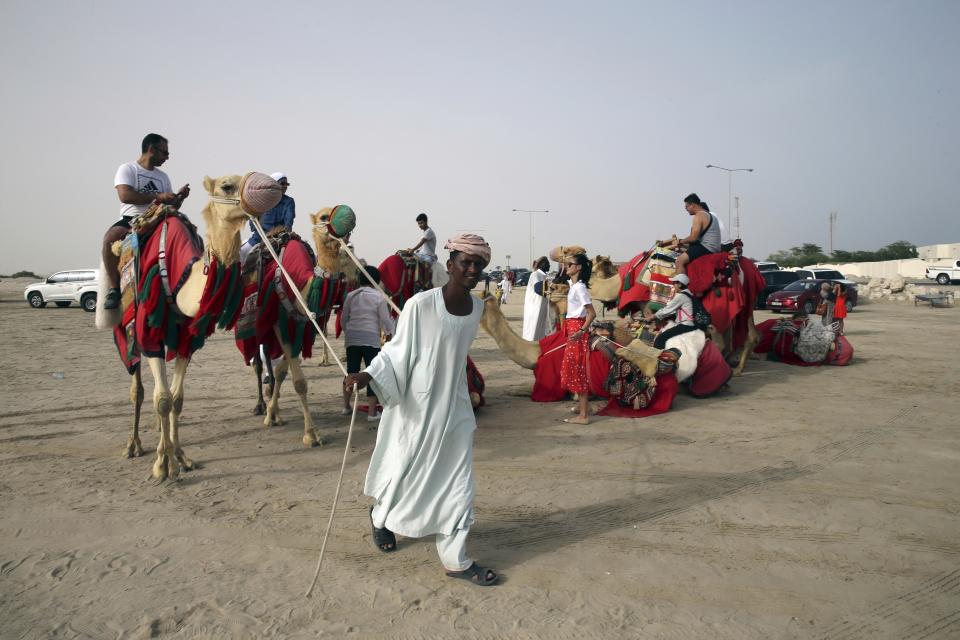 FILE - A camel keeper pulls out camels with tourists on top of them by the sealine road, about 40 kms, 25 miles, south of Doha, Qatar, Friday, April 19, 2019. As many as 1.7 million people could pour into Qatar during the upcoming 2022 FIFA World Cup that begins this November representing over half the population of this small, energy-rich Arab nation. (AP Photo/Kamran Jebreili, File)