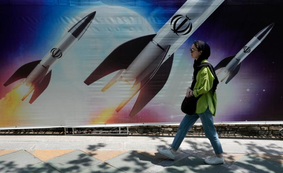 A woman walks past a banner showing missiles being launched, in northern Tehran (Copyright 2024 The Associated Press. All rights reserved)