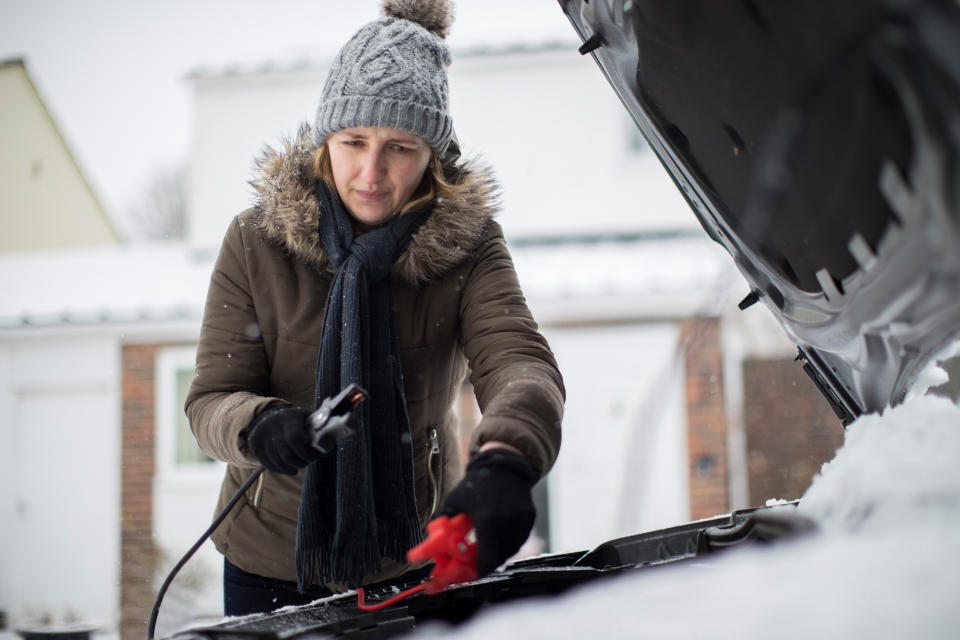 Woman using booster cables to jumpstart her car's battery during winter