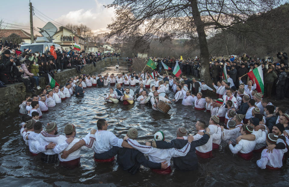 Bulgarians sing, play bagpipes and chain dance in the icy waters of the Tundzha river during Epiphany, in Kalofer, Bulgaria, Monday, Jan. 6, 2020. Thousands of Orthodox Christian worshippers plunged into the icy waters of rivers and lakes across Bulgaria on Monday to retrieve crucifixes tossed by priests in ceremonies commemorating the baptism of Jesus Christ. In the mountain city of Kalofer, in central Bulgaria, dozens of men dressed in white embroidered shirts waded into the frigid Tundzha River waving national flags and singing folk songs. (AP Photo)