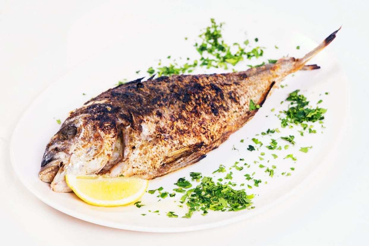 Whole Fish on white plate garnished with fresh chopped herbs and a slice of lemon