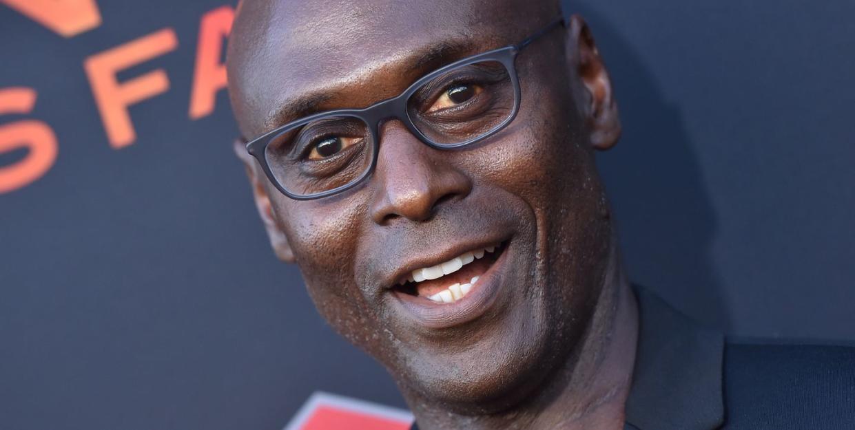 lance reddick, wearing a black suit and black glasses, smiling