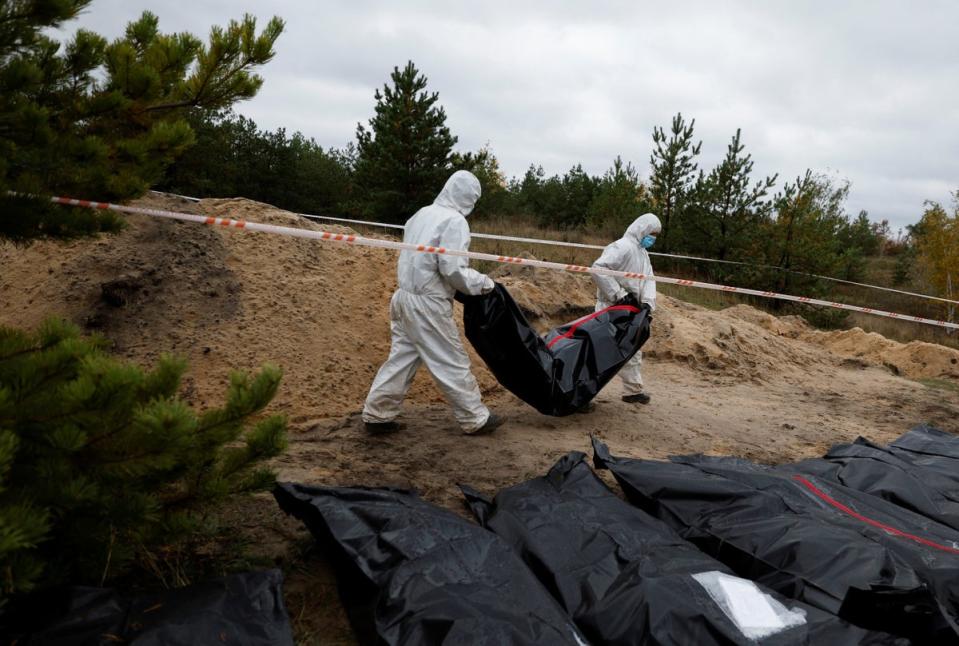 Investigators carry the body of an army officer exhumed from a mass grave in the recaptured town of Lyman, Donetsk (REUTERS)