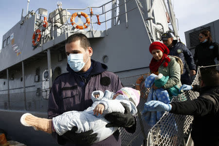 A Greek Coast Guard officer (L) carries a baby from the Agios Efstratios Coast Guard vessel following a rescue operation at open sea, at the port of the Greek island of Lesbos, in this February 8, 2016 file photo. REUTERS/Giorgos Moutafis/Files