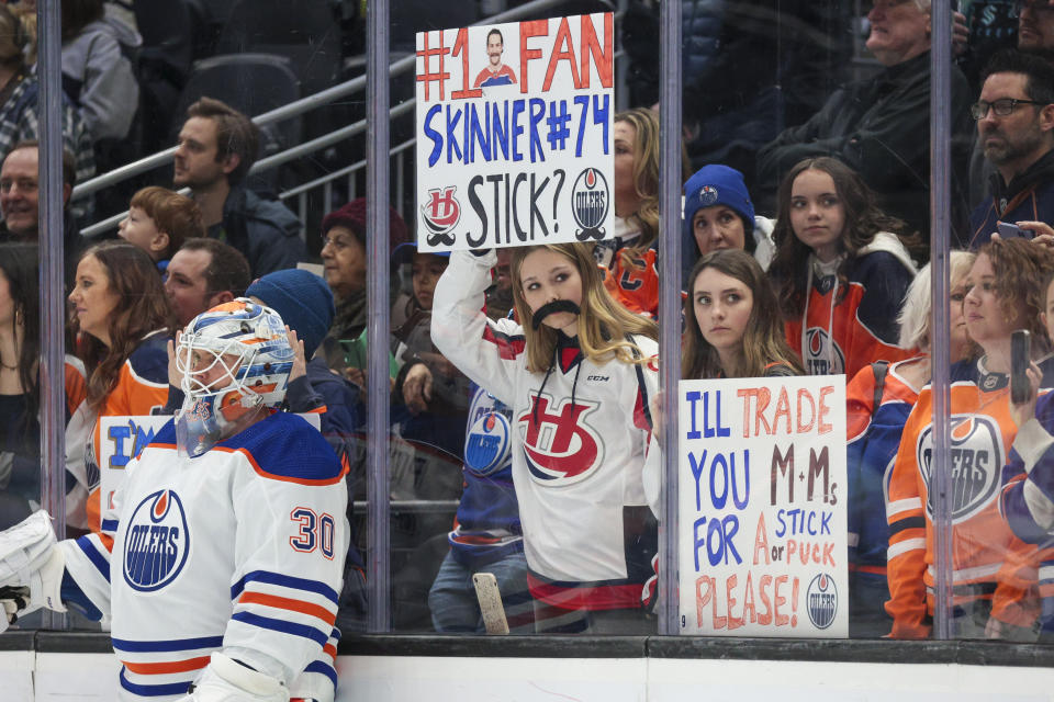 An Edmonton Oilers fan wears a mustache and holds a sign for Edmonton Oilers goaltender Stuart Skinner during warmups before an NHL hockey game against the Seattle Kraken Saturday, March 2, 2024, in Seattle. (AP Photo/Jason Redmond)