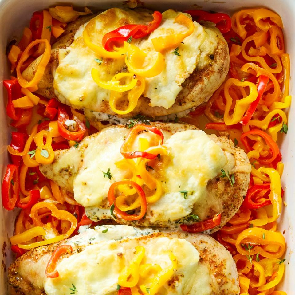 chicken breasts in a casserole dish baked over peppers and topped with cheese