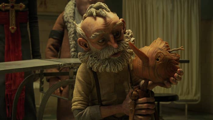 an old man supports the head of a wooden boy from behind