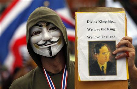 An anti-government protester wears a Gay Fawkes mask and holds a picture of Thailand's King Bhumibol Adulyadej during a rally against the government-backed amnesty bill at the Democracy monument in central Bangkok November 24, 2013. REUTERS/Chaiwat Subprasom