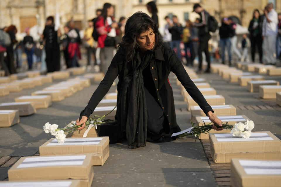 A women places flowers on boxes representing symbolic coffins as she remembers former guerrillas and social leaders who have been killed since the 2016 signing of a peace agreement between rebels of the Revolutionary Armed Forces of Colombia, FARC, and the government, in Bogota, Colombia, Tuesday, Feb. 20, 2024. (AP Photo/Fernando Vergara)