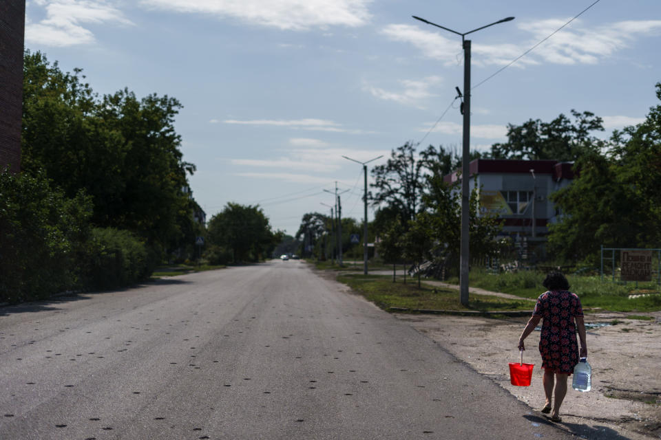 A resident carries water from a well down a road damaged by shrapnel from a May rocket attack in Sloviansk, Donetsk region, eastern Ukraine, Saturday, Aug. 6, 2022. The echo of artillery shells thundering in the distance mingles with the din of people gathered around Sloviansk's public water pumps, piercing the uneasy quiet that smothers the nearly deserted streets of this eastern Ukrainian city. (AP Photo/David Goldman)