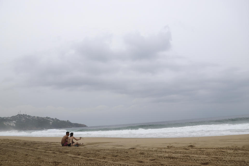 Tourists sit on the beach in Acapulco, Mexico, Tuesday, Oct. 24, 2023. Hurricane Otis has strengthened from tropical storm to a major hurricane in a matter of hours as it approaches Mexico's southern Pacific coast where it was forecast to make landfall near the resort of Acapulco early Wednesday. (AP Photo/Bernardino Hernandez)