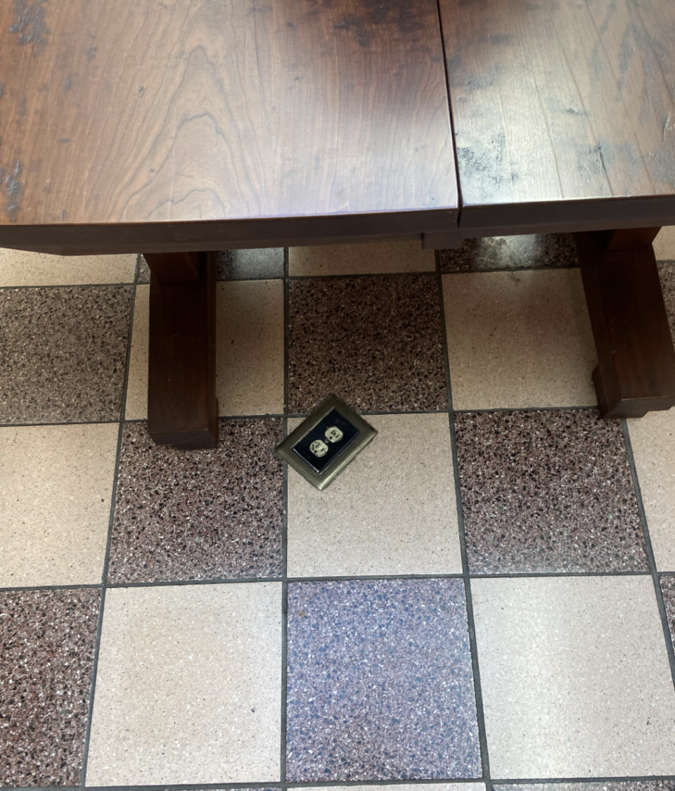 An electrical outlet that is on a floor tile under a table.