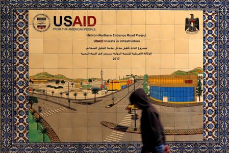 FILE PHOTO: Palestinian walks past a ceramic sign of a USAID project in Hebron in the Israeli-occupied West Bank