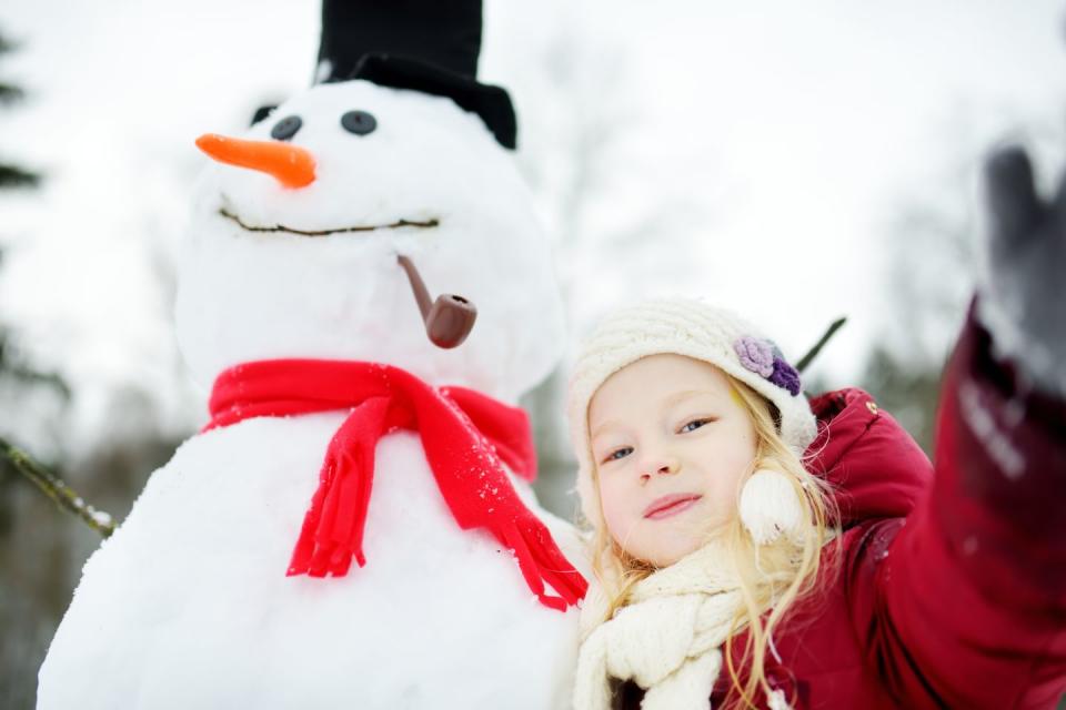 Adorable little girl building a snowman in beautiful winter park. Cute child playing in a snow.