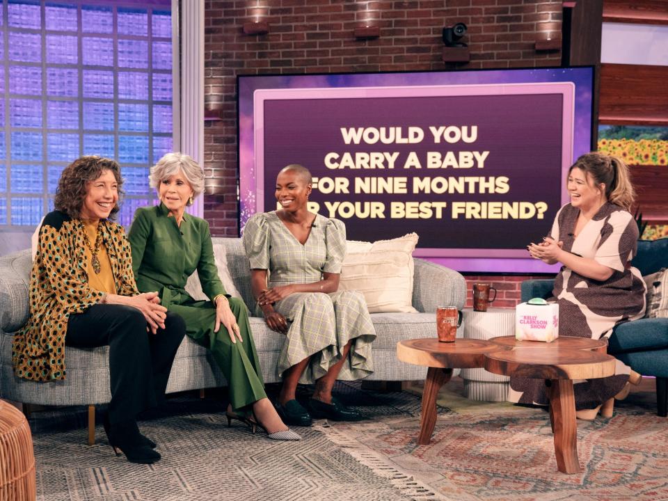 Lily, Jane, and Sasheer laughing on a couch and Kelly laughing on a separate chair. A screen in the background reads, "Would you carry a baby for nine months for your best friend?"