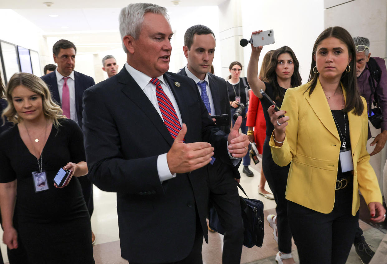 Rep. James Comer talks into a reporter's tape recorder as a crowd of members of the media walks with him down a corridor on Capitol Hill.