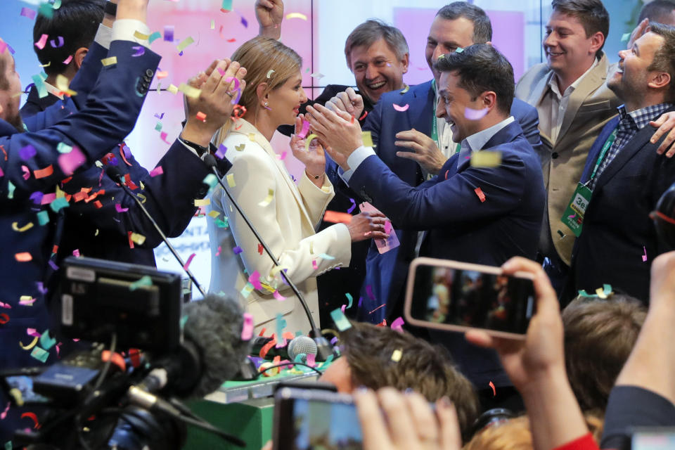 Ukrainian comedian and presidential candidate Volodymyr Zelenskiy, center right, and his wife Olena Zelenska, center left, greet their supporters at his headquarters as the portrait of Ukrainian President Petro Poroshenko is seen on a TV screen, right, after the second round of presidential elections in Kiev, Ukraine, Sunday, April 21, 2019. Ukrainians voted on Sunday in a presidential runoff as the nation's incumbent leader struggles to fend off a strong challenge by a comedian who denounces corruption and plays the role of president in a TV sitcom. (AP Photo/Vadim Ghirda)