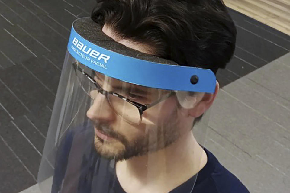 In this March 23, 2020, photo provided by Bauer Hockey Corp., an employee models a medical face shield the hockey equipment manufacturer has begun creating to help those treating the coronavirus pandemic, at Bauer Hockey Corp. in Blainville, Quebec. (Bauer Hockey Corp via AP)