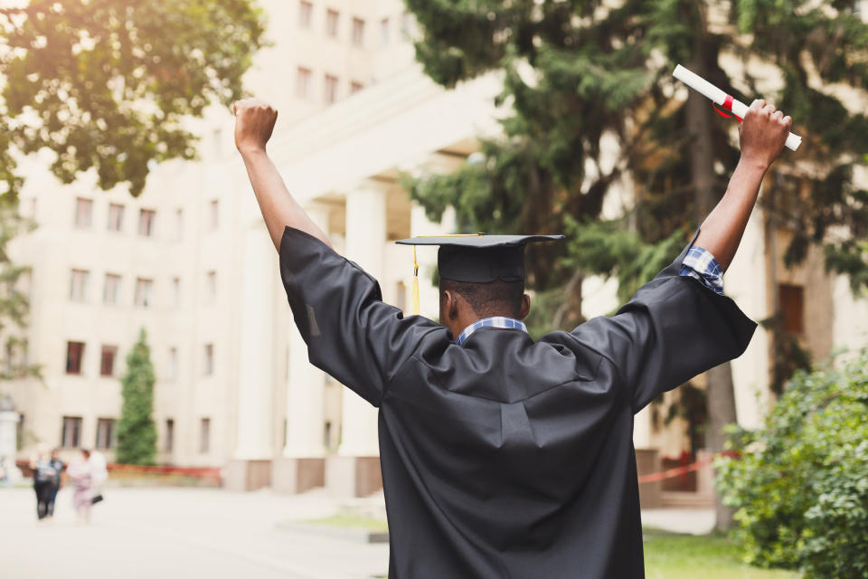 A person holding a diploma and wearing graduation robes celebrates.