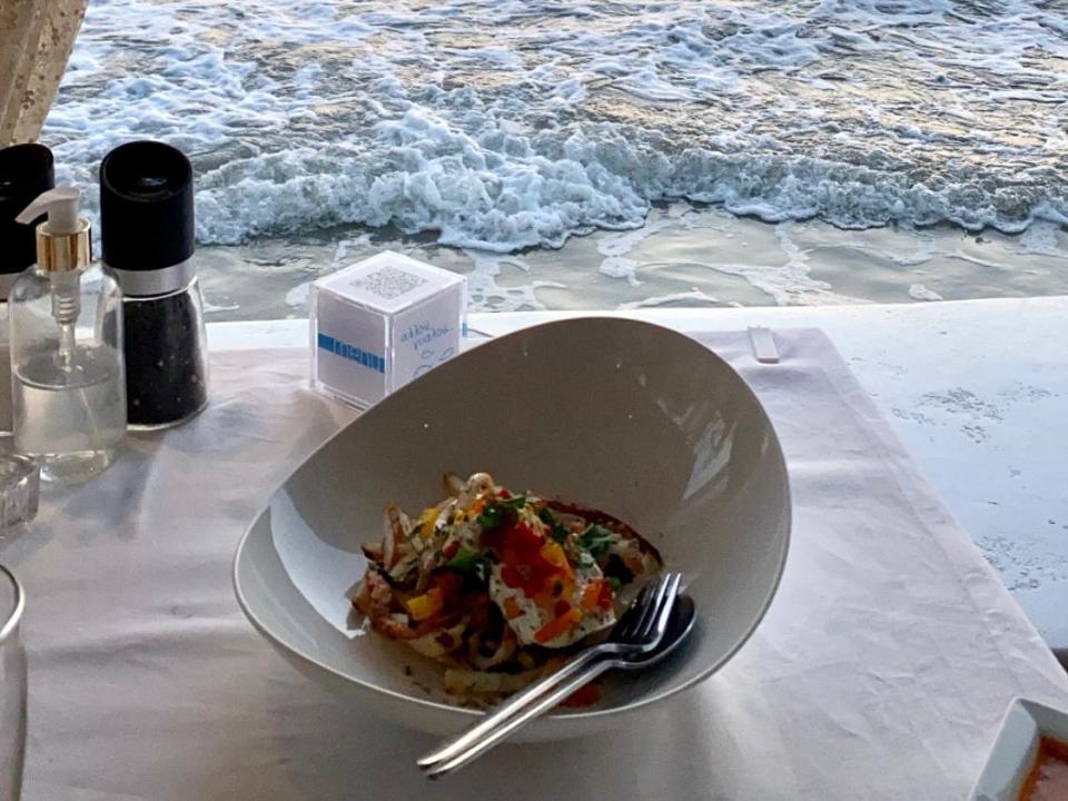 bowl of greek food on a table overlooking the water and a sunset in syros greece