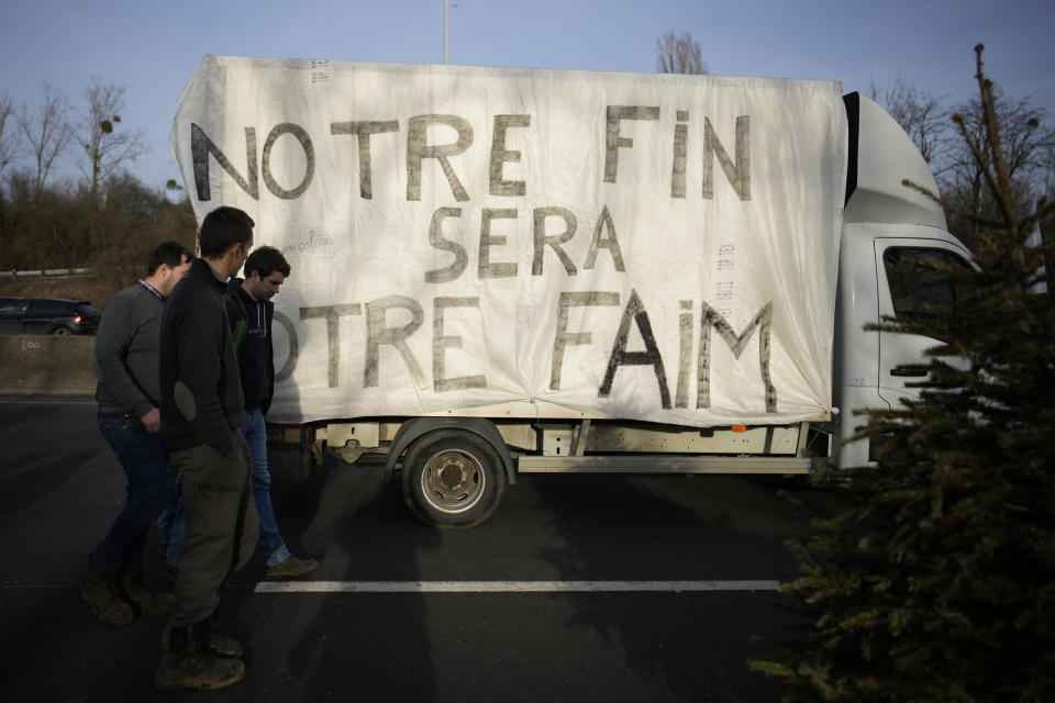 Farmers walk by a truck reading "Our end will be your hunger " on a highway, Monday, Jan. 29, 2024 in Argenteuil, north of Paris. Protesting farmers were encircling Paris with tractor barricades and drive-slows on Monday, using their lumbering vehicles to block highways leading to France's capital to pressure the government over the future of their industry, which has been shaken by repercussions of the Ukraine war. (AP Photo/Christophe Ena)