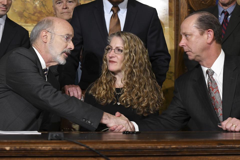 Pennsylvania Gov. Tom Wolf of Pennsylvania shakes hands with Jim Piazza after signing anti-hazing legislation inspired by Piazza's son, Penn State student Tim Piazza who died after a night of drinking in a fraternity house, Friday, Oct. 19, 2018 in Harrisburg, Pa. Sitting between them is Evelyn Piazza, the mother of Tim Piazza. (AP Photo/Marc Levy)