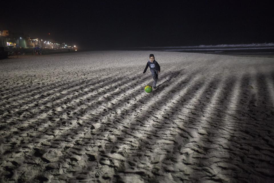 A boy plays soccer at the Mexican side of the border with the U.S. at the Pacific Ocean, Tijuana, Mexico, Friday, Nov. 16, 2018. With about 3,000 Central American migrants having reached the Mexican border across from California and thousands more anticipated, the mayor of Tijuana said Friday that the city was preparing for an influx that will last at least six months and may have no end in sight. (AP Photo/Rodrigo Abd)