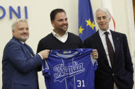 Hall of Fame catcher Mike Piazza shows his jersey during his presentation as Italy's national baseball team coach, at the Italian Olympic Committee headquarters in Rome, Friday, Nov. 29, 2019. At right is Olympic Committee president Giovanni Malago' and at left is the President of the Italian Baseball Federation Andrea Marcon. (AP Photo/Alberto Pellaschiar)