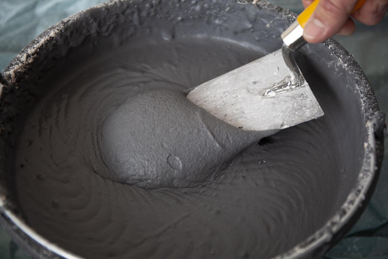 Hand of worker with a trowel in a bucket with concrete plaster