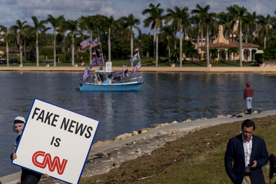 A man walks behind an on-air reporter holding a sign that reads “Fake News is CNN” outside President Donald Trump’s club, Mar-a-Lago, in Palm Beach on Nov. 15, 2022. | Andrew Harnik, Associated Press