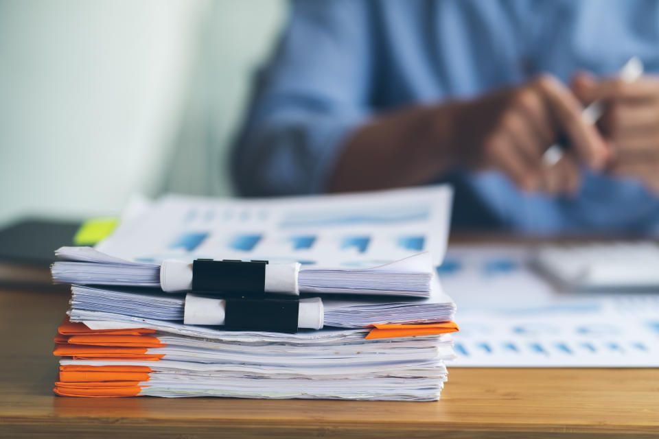 Businesswoman working in stacks of paperwork files for searching infomation unfinished documents about pile audit form on desk office and investigate financial doc in busy workload