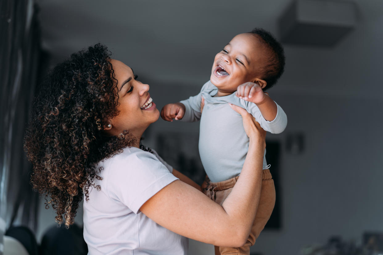 Shot of a beautiful young mother having fun at home with her cute little baby son. Little boy being lifted up by mother in the living room at home.