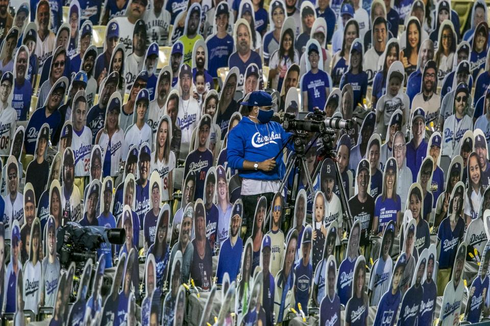 A man and his camera are perched in stadium seating amid numerous cardboard likenesses of fans.