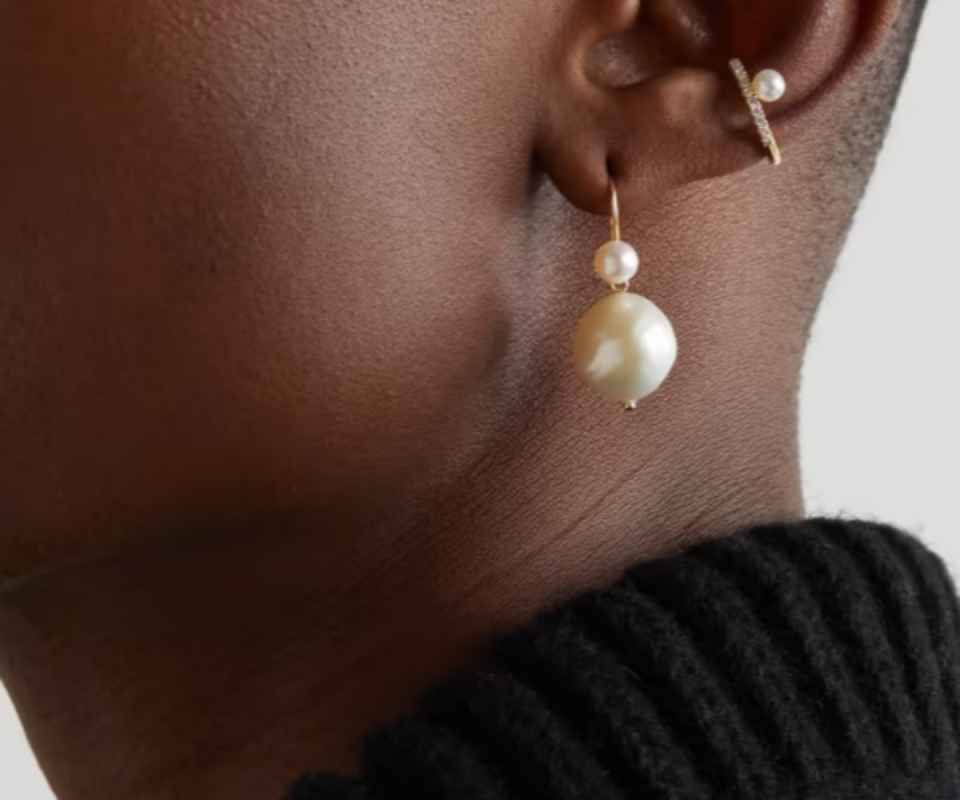 A close up of a woman of African descent wearing pearl drop earrings with a black turtle neck jumper.