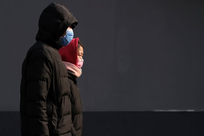 People wearing protective masks walk along a street in Beijing