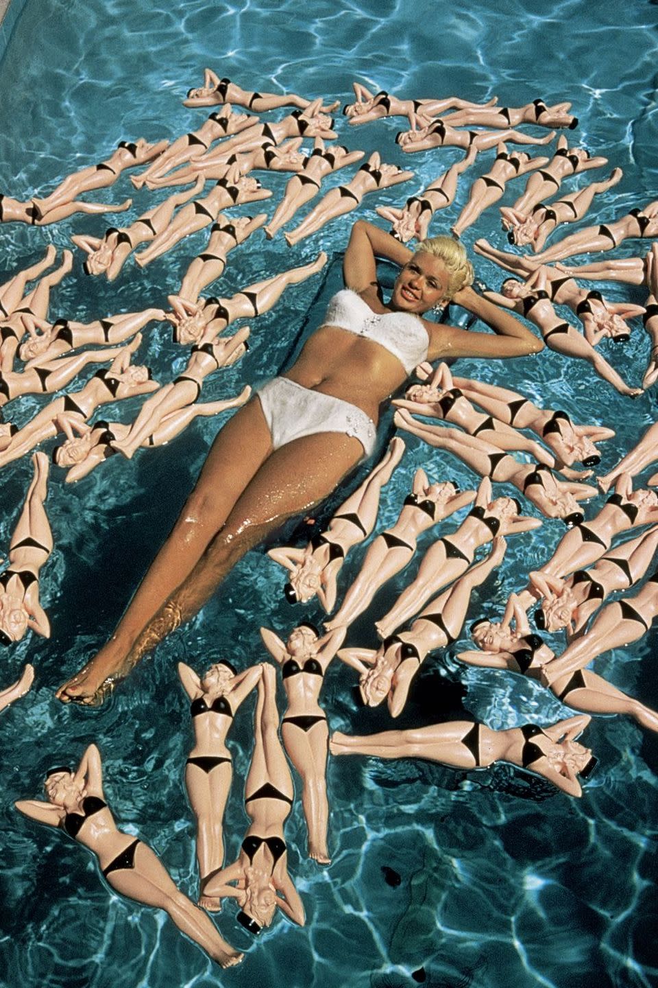 <p>Jayne Mansfield poses on an inflatable raft surrounded by bottles shaped like bikini-clad versions of herself in 1957.</p>