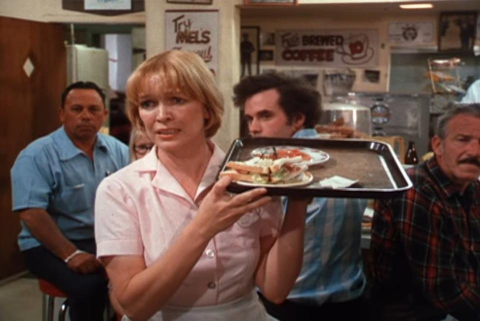 Ellen Burstyn wears a waitress's uniform and carries a tray