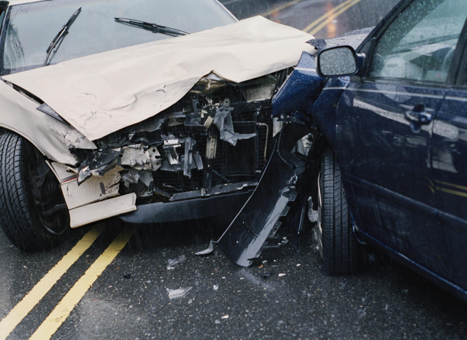 Two cars after a collision on a rainy road. Both vehicles have significant front-end damage. No people are visible