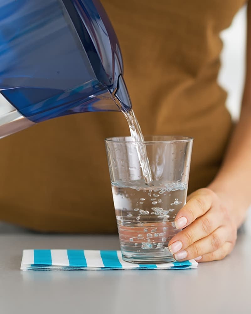 Closeup on housewife pouring water into glass from water filter pitcher