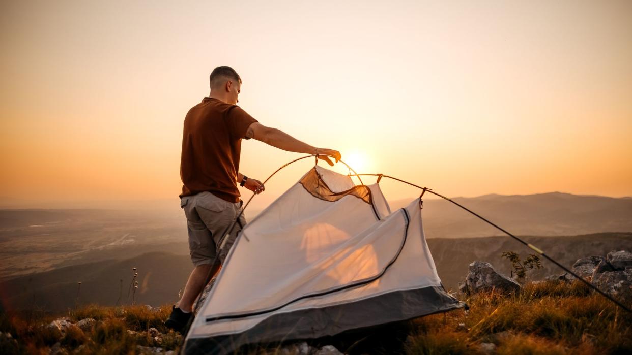  A man setting up his tent on a hill. 