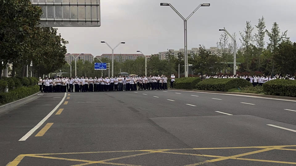 In this photo released by Yang on Sunday, July 10, 2022, plain clothes securities stand on the road as people stage a protest at the entrance to a branch of China's central bank in Zhengzhou in central China's Henan Province. A large crowd of angry Chinese bank depositors faced off with police Sunday, some reportedly injured as they were roughly taken away, in a case that has drawn attention because of earlier attempts to use a COVID-19 tracking app to prevent them from mobilising. (AP Photo/Yang)