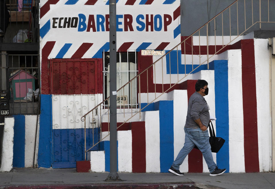 FILE — In this Friday May 8, 2020 file photo A pedestrian wears a mask as he walks past the closed Echo Barber Shop in the Echo Park neighborhood of Los Angeles. California Health and Human Services Secretary Dr. Mark Ghaly explained the math behind the state's calculation of when it is safe to lift it's stay-at-home order and overnight curfew, during a news briefing Tuesday, Jan. 26, 2021. (AP Photo/Damian Dovarganes, File)