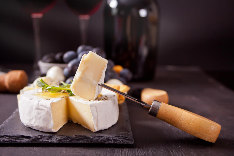 Cheese camembert brie on the board, two glasses and bottle of red wine.